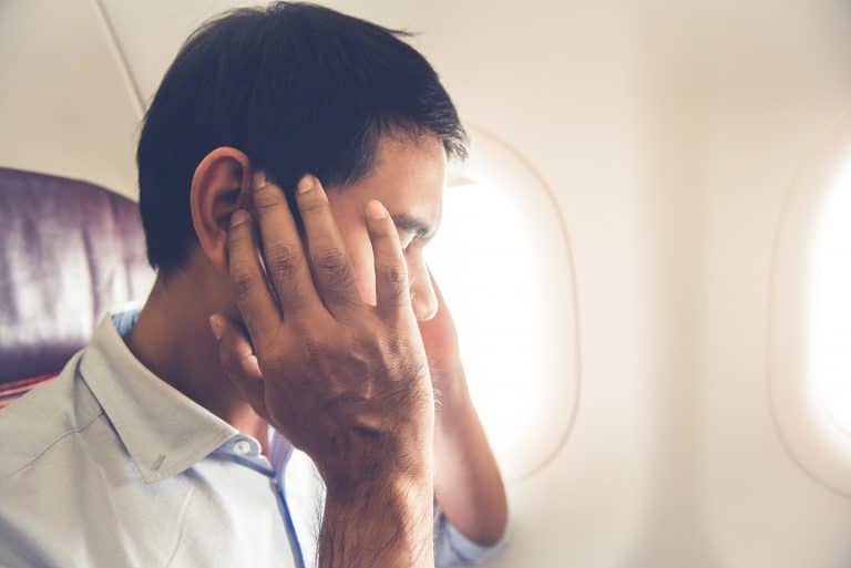 Man on airplane experiencing ear troubles.