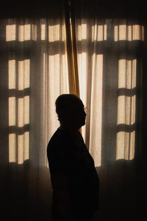 A silhouette of a person standing close to a window indoors.
