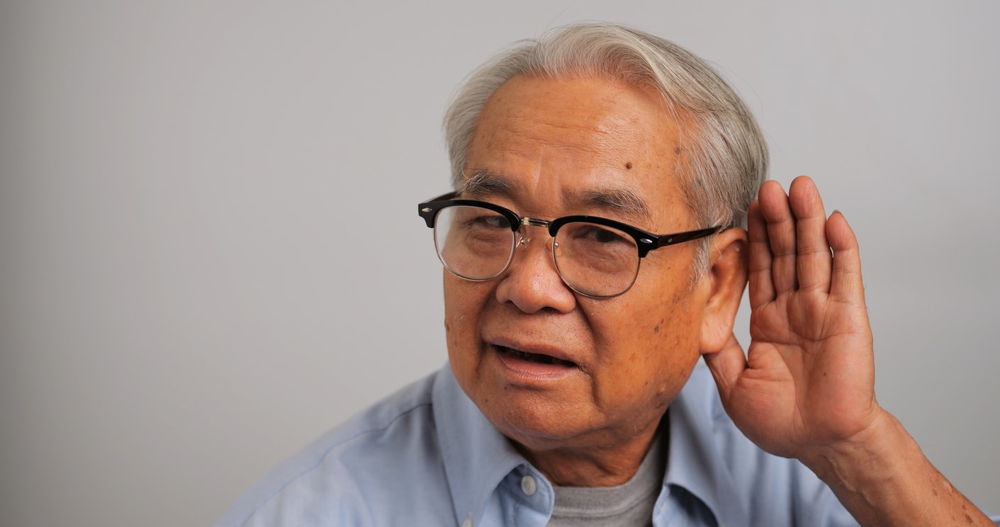 Man with hearing loss gestures behind ear