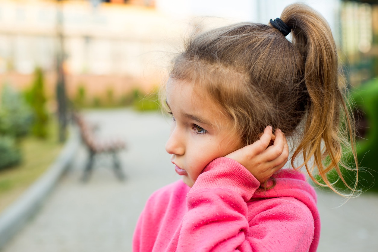 Young child experiencing muffled hearing holds her ear.