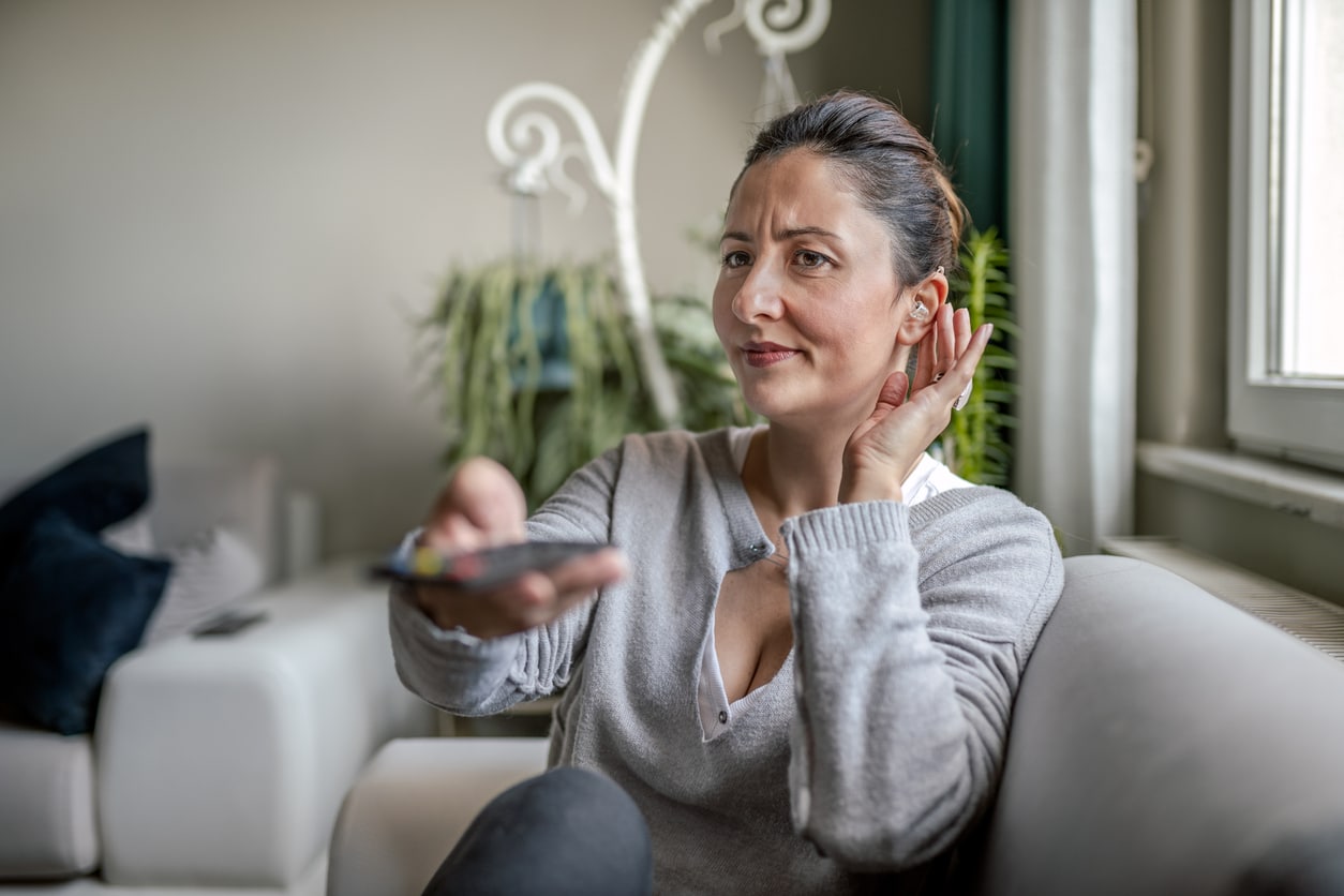 Woman with hearing loss turning the volume up on the tv